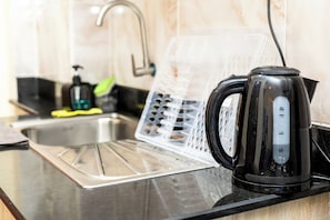 A kitchen with a kettle, a sink, and a dish rack. - Transit Hub: 5min to Wilson • 20min JKIA • Secure Parking • WiFi (Nairobi)