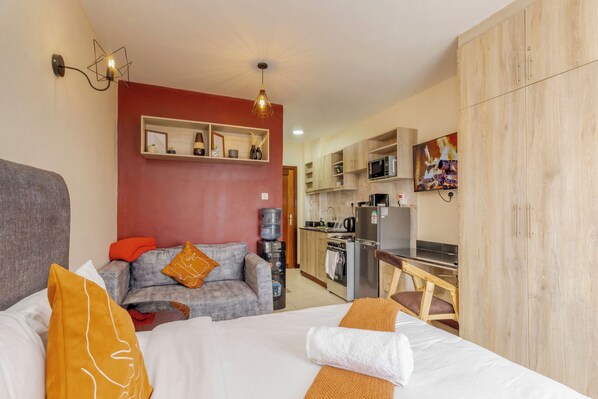 A compact hotel room with a bed, a sofa, a kitchenette, and a wooden wardrobe. - Transit Hub: 5min to Wilson • 20min JKIA • Secure Parking • WiFi (Nairobi)