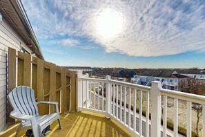 Un balcón con barandilla blanca, una silla Adirondack y vista a una zona residencial.