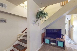 Una escalera con barandilla de madera, una planta en la pared, un televisor de pantalla plana y un mueble bajo.