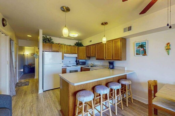 Una cocina con armarios de madera, una isla central con taburetes, un refrigerador e iluminación colgante.