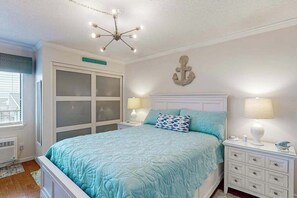 Ein Schlafzimmer mit Bett, Nachttischlampen, einer Chandelierleuchtre, einem Wanddekor und einem Fenster mit Jalousien.