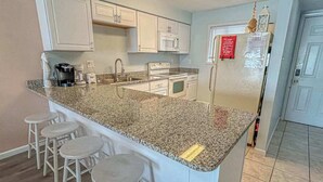 A kitchen with white cabinets, a granite countertop, a refrigerator, and a microwave. - Blaire Isle 302N (Ocean City)