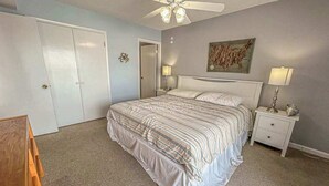 A bedroom with a bed, a nightstand, a ceiling fan, a door, and a wall-mounted artwork. - Blaire Isle 302N (Ocean City)