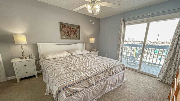 A bedroom with a bed, two bedside tables, a ceiling fan, a large window with a view, and a painting on the wall. - Blaire Isle 302N (Ocean City)
