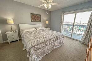 A bedroom with a bed, two bedside tables, a ceiling fan, a large window with a view, and a painting on the wall. - Blaire Isle 302N (Ocean City)