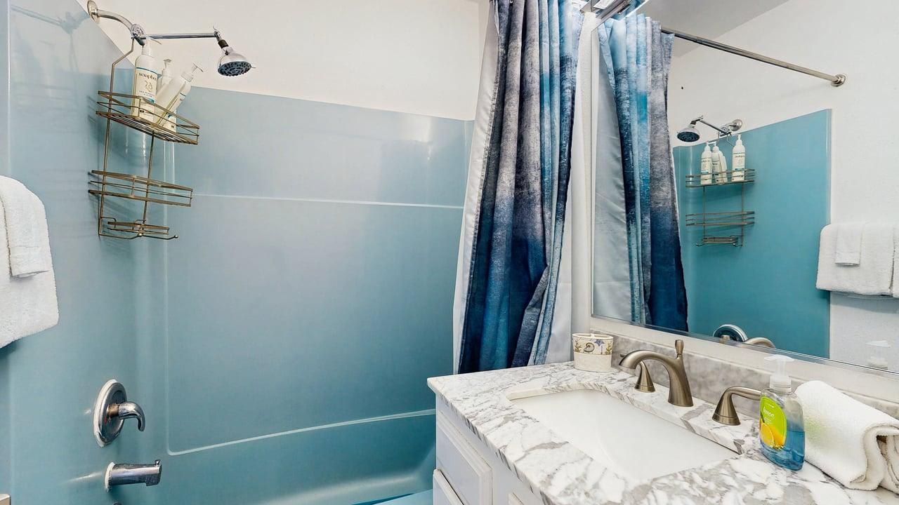 Un baño con ducha, un lavamanos de encimera de mármol y un espejo.