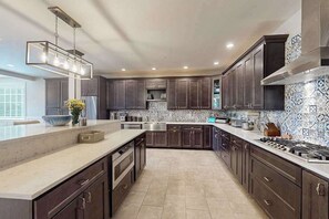 A modern kitchen with dark cabinets, a large island, stainless steel appliances, and a patterned backsplash. - 3 Ladies Estate (Bishopville)