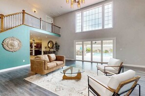 A spacious living area with a high ceiling, a staircase, a large window, and a view of an outdoor pool. - 3 Ladies Estate (Bishopville)