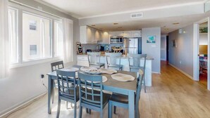 Una cocina moderna con armarios blancos, una isla central y un comedor con sillas azules y una mesa.