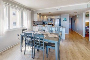 A modern kitchen with white cabinets, a central island, and a dining area with blue chairs and a table. - Oceanfront Condo with Balcony, Beach Access, Central AC, WiFi & Washer/Dryer (Ocean City)