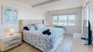 Un dormitorio con cama, escritorio, silla, televisor y ventana con vista al mar.