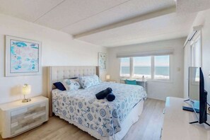 A bedroom with a bed, a desk, a chair, a TV, and a window with a view of the sea. - Oceanfront Condo with Balcony, Beach Access, Central AC, WiFi & Washer/Dryer (Ocean City)