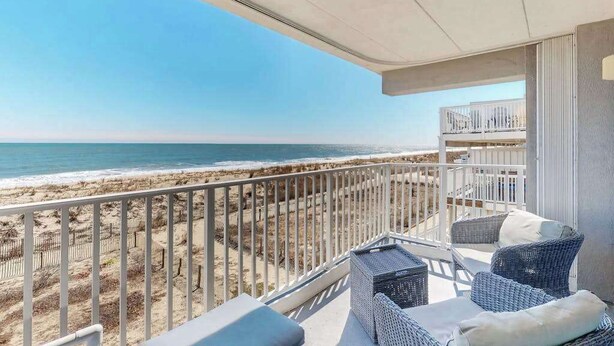 Un balcón con mobiliario de mimbre, vista a la playa y barandilla.