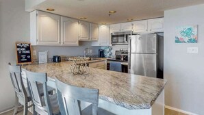 Una cocina con armarios blancos, un refrigerador de acero inoxidable y una encimera de mármol.