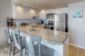 A kitchen with white cabinets, a stainless steel refrigerator, and a marble countertop. - Oceanfront Condo with Balcony, Beach Access, Central AC, WiFi & Washer/Dryer (Ocean City)