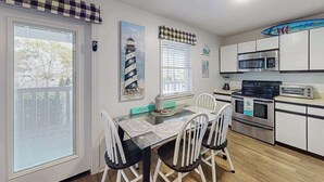 A kitchen with a dining table, chairs, a microwave, a stove, and a surfboard decoration. - Marathon North 103 (Ocean City)