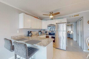 A kitchen with white cabinets, a granite countertop, a refrigerator, a microwave, and a ceiling fan.
