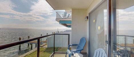 A balcony with a view of the water, two chairs, and a wicker basket.