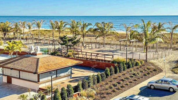 Ein modernes Gebäude mit flachem Dach, umgeben von Palmen und Blick auf einen Strand.