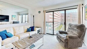 Ein modernes Wohnzimmer mit Sofa, Sessel, Couchtisch und einem großen Fenster mit Blick auf ein Gebäude.