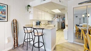 Eine moderne Küche mit weißen Schränken, einer zentralen Kochinsel mit Sitzgelegenheiten und einem Essbereich mit Holzkästen.