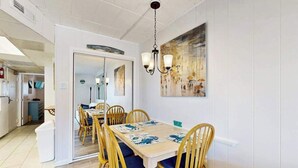 Ein Essbereich mit einem für vier Personen gedeckten Tisch, Holzstühlen, einer Pendelleuchte und einem Gemälde an der Wand.