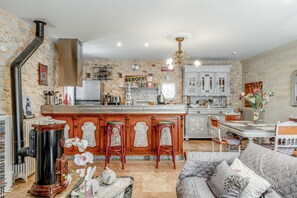 Una cocina con pared de piedra, una isla central con taburetes, un refrigerador y un letrero que dice 'BERGER'.