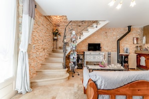 Una escalera conduce a un dormitorio tipo loft con una cama, un televisor y una pequeña mesa con objetos encima.