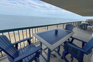 Ein Balkon mit Tisch und Stühlen, der Blick auf einen Strand bietet.