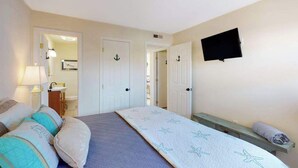 Een slaapkamer met een bed, nachtkastje, tv aan de muur en een deur naar een andere kamer.