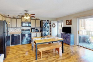 A compact kitchen with modern appliances, a dining area with a wooden table and bench, and a large window with a view. - Nautical-themed condo with a balcony, open-layout, & W/D - steps from the sand (Ocean City)