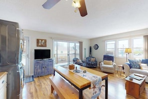 A spacious living area with a wooden bench, a television, and a dining table. - Nautical-themed condo with a balcony, open-layout, & W/D - steps from the sand (Ocean City)