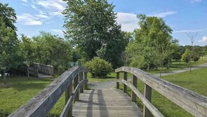 A wooden bridge leading to a grassy area with trees. - Teal Haven (Ocean Pines)