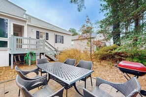A patio with a table and chairs, a barbecue grill, and a house with a covered deck.