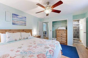 A bedroom with a bed, a ceiling fan, a dresser, and a bathroom with a shower.