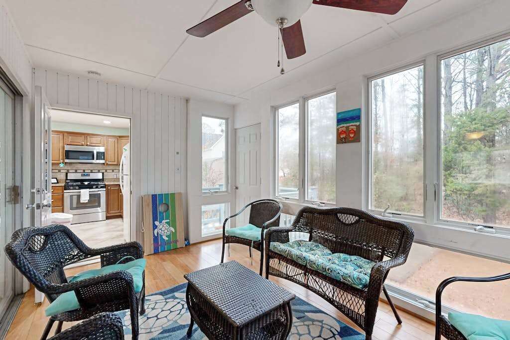 A sunlit room with wicker furniture, a ceiling fan, and large windows.