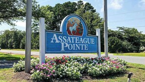 Schild für Assateague Pointe mit dem Pferde-und-Baum-Logo, umgeben von Blumen.