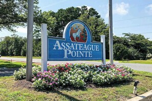 Schild für Assateague Pointe mit dem Pferde-und-Baum-Logo, umgeben von Blumen.