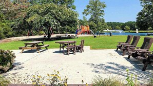 Ein Park mit Picknicktischen, Liegestühlen, einem Spielplatz und einem See.
