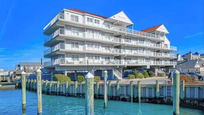 Een meerlaags hotel aan het water met balkons, een steiger en een helderblauwe lucht.