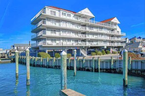 Ein mehrstöckiges Hotel am Wasser mit Balkonen, einem Anlegesteg und blauem Himmel.