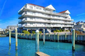 A multi-story waterfront hotel with balconies, a dock, and a clear blue sky. - Lovely condo with water view, pool, balcony, fast WiFi, & washer/dryer (Ocean City)