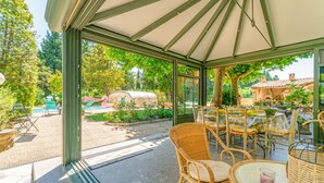 Una veranda coperta con mobili in vimini, un tavolo con un bicchiere e vista su un giardino e un rimorchio.