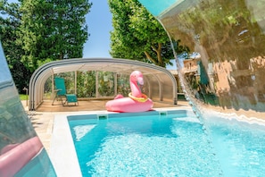A swimming pool with a transparent cover, a pink flamingo float, and a glass enclosure with a chair. - Family Cottage with Shared Heated Pool, Wi-Fi, and Air Conditioning in Le Thor (Le Thor)
