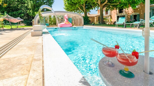 Una piscina con un gonfiabile a forma di fenicottero rosa, lettini prendisole e un drink con cannuccia e fragola.