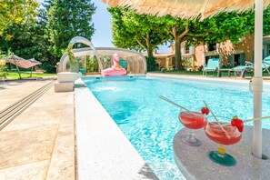 Une piscine avec un flotteur en forme de flamant rose, des chaises longues et un verre agrémenté d’une paille et d’une fraise.