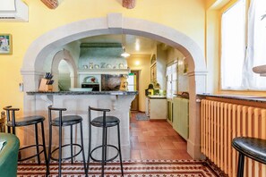 Una cocina con un arco, taburetes de bar, un refrigerador y una ventana con cortinas.