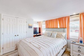 Une chambre à coucher avec un lit, une télévision, une commode et une fenêtre avec des rideaux.