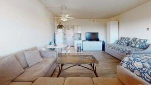 A living room with a sofa, a coffee table, a TV, and a ceiling fan. - Comfortable ocean-view studio with pool (Ocean City)
